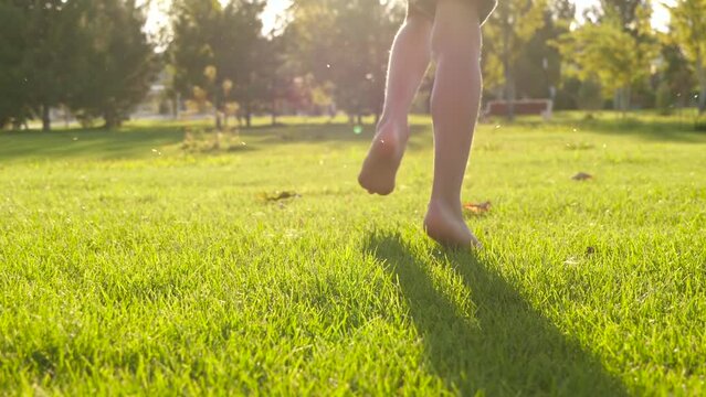 Kids legs are running close-up on the green grass. A boy runs with his bare feet through a meadow, a park. happy family kid concept. Chil dreams, city park game
