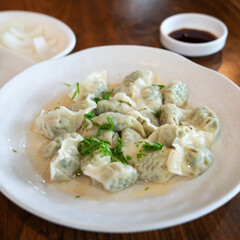 Fresh, delicious boiled garlic chives dumplings, jiaozi in white plate on wooden table background.