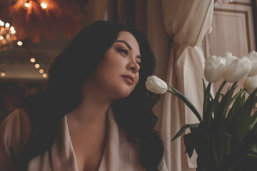 Beautiful woman drressed biege elegant suit sit in cafe and drink the cup of coffee. The plus size woman holding a bouquet of whine flowers. Happy overweight model