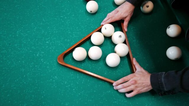 caucasian male racking white balls in triangular rack in a russian pyramide billiard.