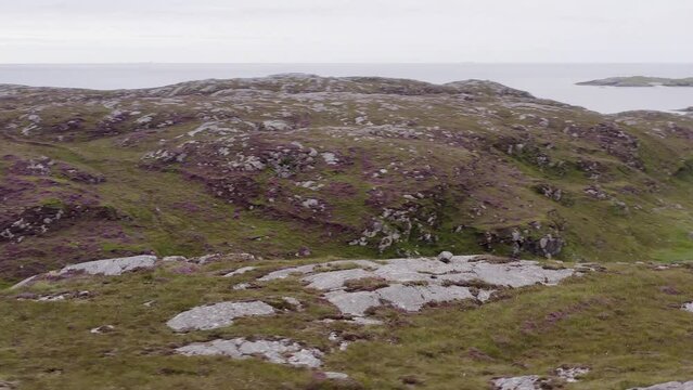 Drone shot circling the cemetery and Iron Age House at Bosta beach on the Isle of Bernera, near the Isle of Lewis on the Outer Hebrides of Scotland. Ocean, hills, moorland and peatland are visible.