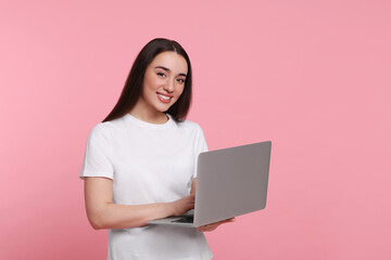 Naklejka premium Smiling young woman working with laptop on pink background, space for text