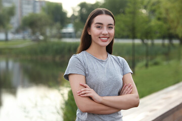 Portrait of beautiful woman with crossed arms outdoors. Attractive lady smiling and looking into camera. Space for text