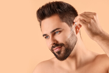 Obraz premium Handsome man applying cosmetic serum onto face on beige background, space for text