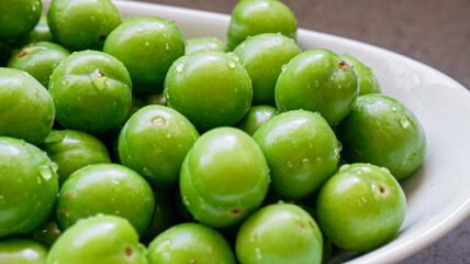 Green sour white bowl , washed plums with water drops, green isolated plums, green sour white bowl ,top view of full  on a isolated grey background, fruit concept idea photo.