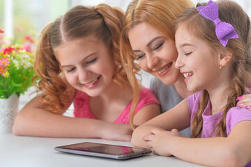 Mother and girls sitting at table and using laptop