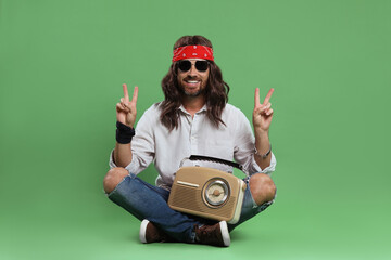 Stylish hippie man with radio showing V-sign on green background