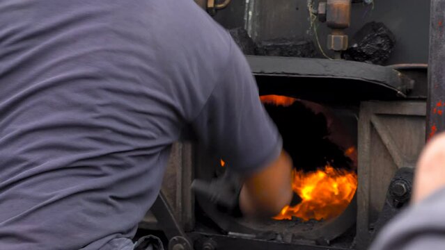 train driver shovelling coal into the furnace boiler in the toy train to generate steam for this antique tourist attraction and then closing it