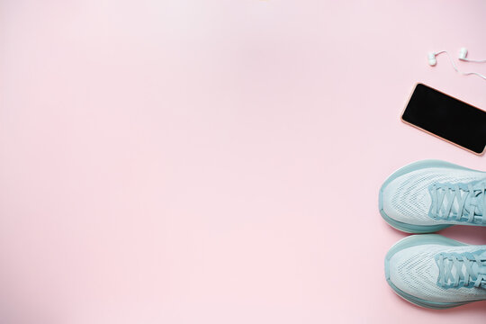 New female modern running shoe with phone and headphones on empty pink background. Stylish monochrome shoes for active people that incorporate new health technology. Top view