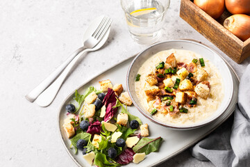 cheesy leek soup with croutons, bacon and fresh lettuce leaves on a wooden table.