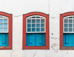Fototapeta na wymiar Decorative windows, blue and red, colonial, vintage, on a white wall with cracks. Brazilian colonial old houses