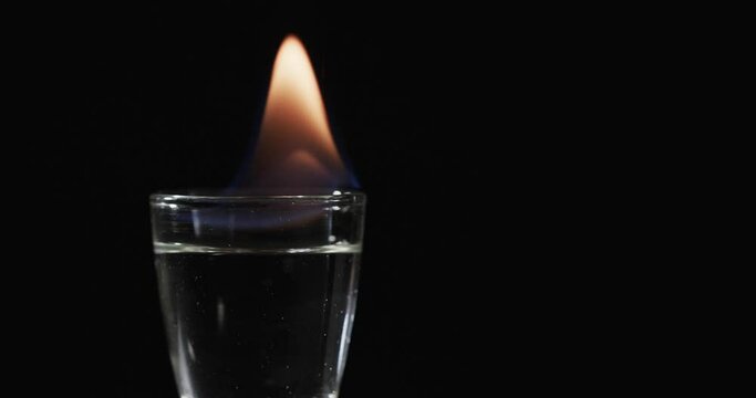 Video of lit alcohol in glass with orange fire flame and copy space on black background