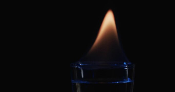 Video of lit alcohol in glass with orange fire flame and copy space on black background