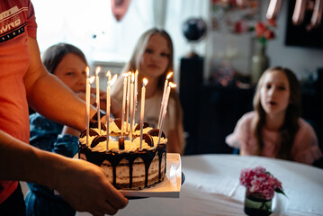 Friends and relatives of the girl gathered at the table while she makes a wish and blows out the candles