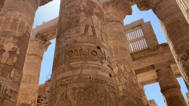 Karnac temple, Egypt.  Circular pan of painted and carved hieroglyphics in colossal columns.  Pan up to ceiling ruins and sky.