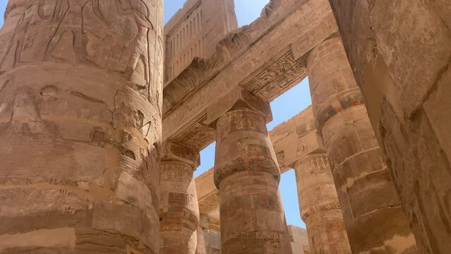 Karnac temple in Egypt.  Circular pan, colossal columns with ancient hieroglyphics painted and engraved. Sunny day. Reflected golden light.