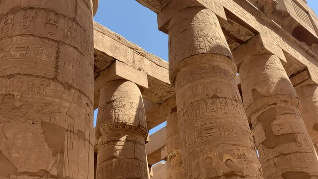 Karnac temple, Egypt. Slow pan out of massive ancient columns painted and engraved with hieroglyphics. Sunny day, blue sky.