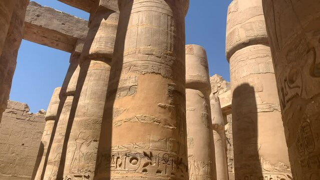 Karnac temple, Egypt.  Circular pan to right, massive ancient columns painted and engraved with hieroglyphics, show repair patches.  Sunny day, reveal of scaffolding in the background.