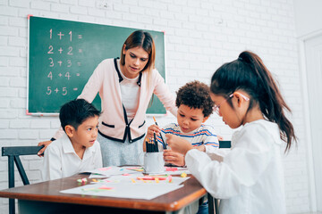 Fototapeta premium Happy school teacher and students having interesting engaging activities in class. Little children sitting around classroom table, talking and playing fun games together.
