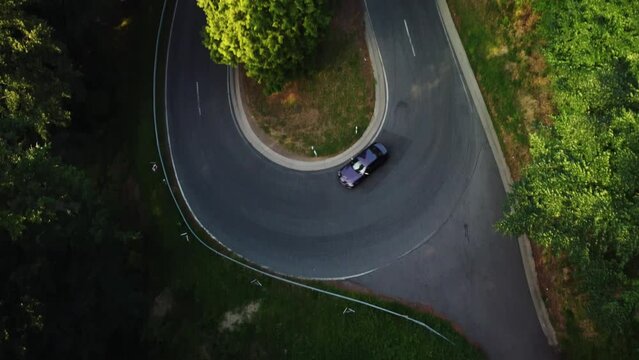 Drone shot of the car taking a sharp turn in the green forest in summer