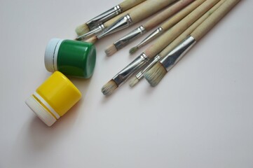 Gouache paints in closed jars and brushes on a white background. Items for drawing, creativity, hobby.