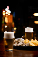 Happy hour in a pub with a closeup of pints of beer and a portion of finger food with potatoes and sausages on a blurred background