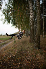 a beautiful girl swings on a swing in the middle of an autumn birch forest. autumn atmosphere in the forest
