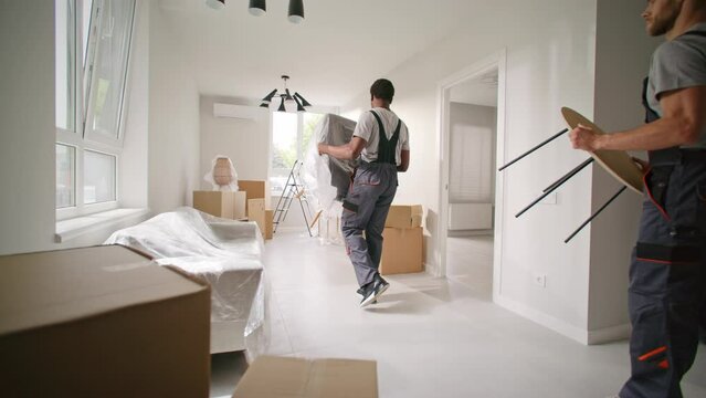 Three multiethnic contractors arranging furniture in repaired apartment. Repairmen carrying tools box. Repair masters talking at modern updated flat. Craftsmen finisged apartment renovatiom.