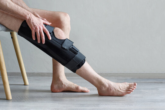 Knee Brace on male leg on grey background. Orthopedic Anatomic Orthosis. Braces for knee fixation, injuries and pain. Foot orthosis tutor