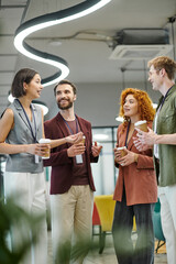 young businesswoman talking to cheerful colleagues with paper cups, coffee break in modern office