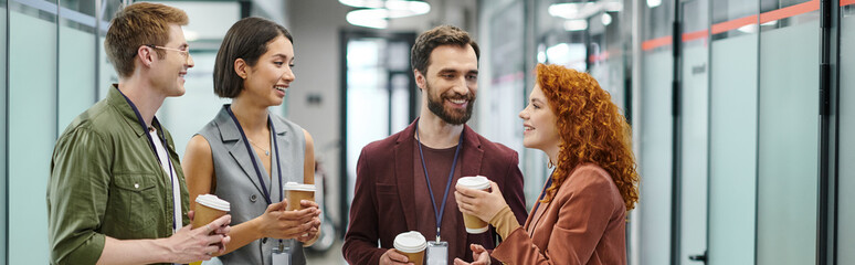 cheerful business colleagues with paper cups talking in coworking office, coffee break