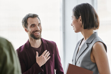 grateful bearded entrepreneur touching chest near young businesswoman in modern office