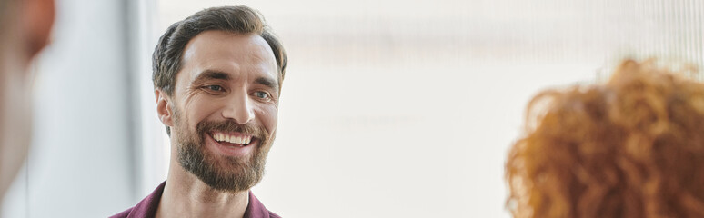 cheerful bearded businessman near colleagues on blurred foreground in office, banner