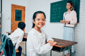 portrait of smiling little child looking at camera while posing confidently sitting in school classroom, copy space.