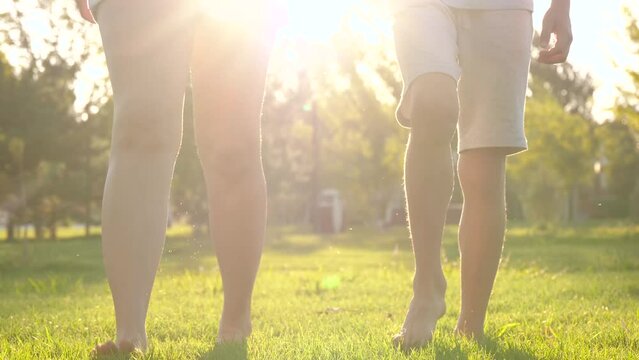 Mom and son are walking on the green grass with bare feet. A happy family is playing in the park on the green grass. Kid legs close up. Happy family, walk, dreams