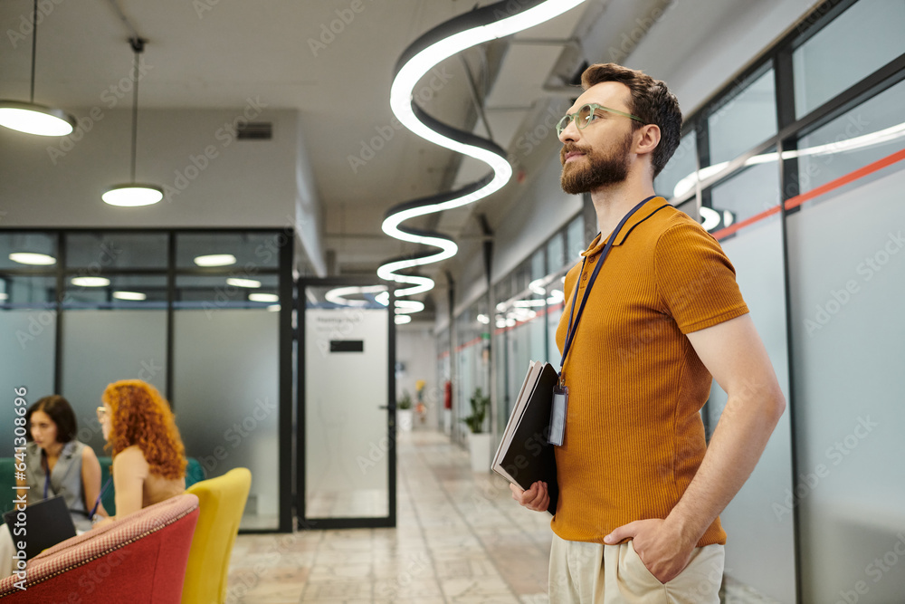 Wall mural confident bearded business standing with documents, businesswomen talking on blurred background