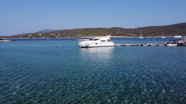Young man walking in shallow water and a Yacht boat moored to wooden jetty dock in Blue lagoon, Veliki Budikovac island. Aerial