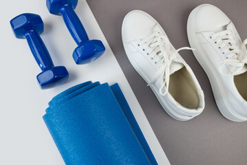 close-up of a rolled up blue color yoga mat, white sneakers, dumbbells, healthy lifestyle, sport and exercise concept.