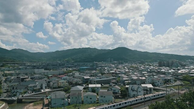 [Drone] Looking down on a commuter train running through a residential area in midsummer