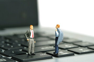Miniature tiny people toy figure photography. Business talk concept illustration. Two businessman have a conversation, standing above laptop notebook.