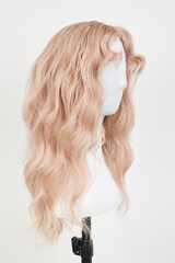 Natural looking blonde wig on white mannequin head. Long hair on the plastic wig holder isolated on white background.