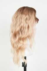Naklejka premium Natural looking blonde wig on white mannequin head. Long hair on the plastic wig holder isolated on white background, side view.