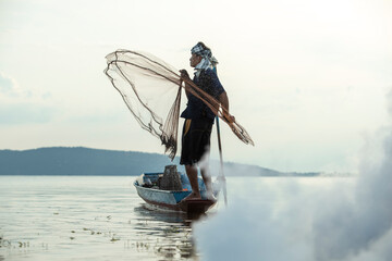 Middle aged Asian fisherman while throwing fishing net from boat on the lake, Thailand countryside. © Pituk