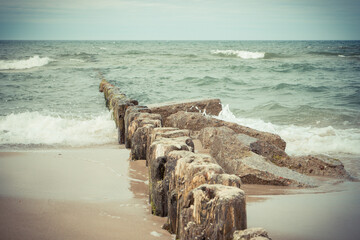 Scenic view of wooden breakwaters and sea waves at beach. Stormy day at sea