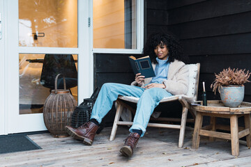 leisure, literature and people concept - smiling hispanic american woman reading book outdoor home