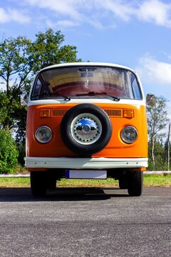 Oostmalle, Belgium - August 19 2023: An orange and white vintage old timer volkswagen split bus, minivan, minibus or camper standing parked on the street. The VW car has a spare tire at the front.