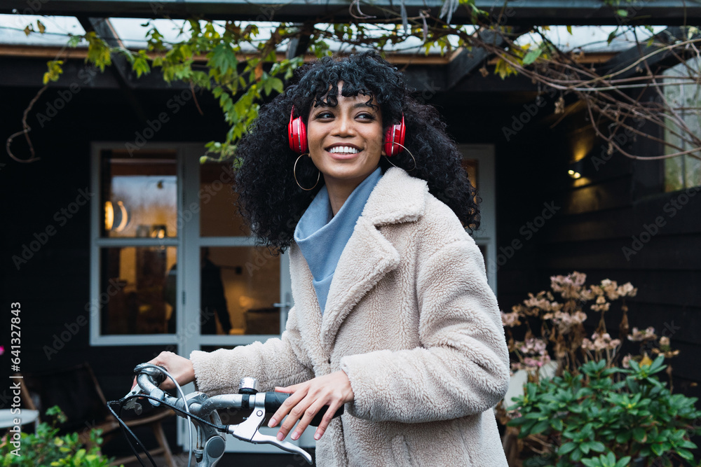 Poster smiling hispanic woman listening to music with headphones riding a bicycle