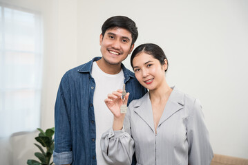 Happy young family couple holding key to new home on moving day concept, first time real estate owners man husband and woman wife look at camera.