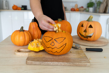 Female hands gutting Halloween pumpkin. Woman hollowing Jack-o'-lantern, removing guts and seeds from a Halloween pumpkin by reaching inside through the cut-off top lid.