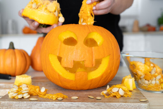 Female hands gutting Halloween pumpkin. Woman hollowing Jack-o'-lantern, removing guts and seeds from a Halloween pumpkin by reaching inside through the cut-off top lid.